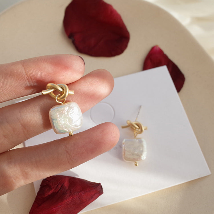 Boucles d'oreilles en perle naturelle sur fond beige avec pétales