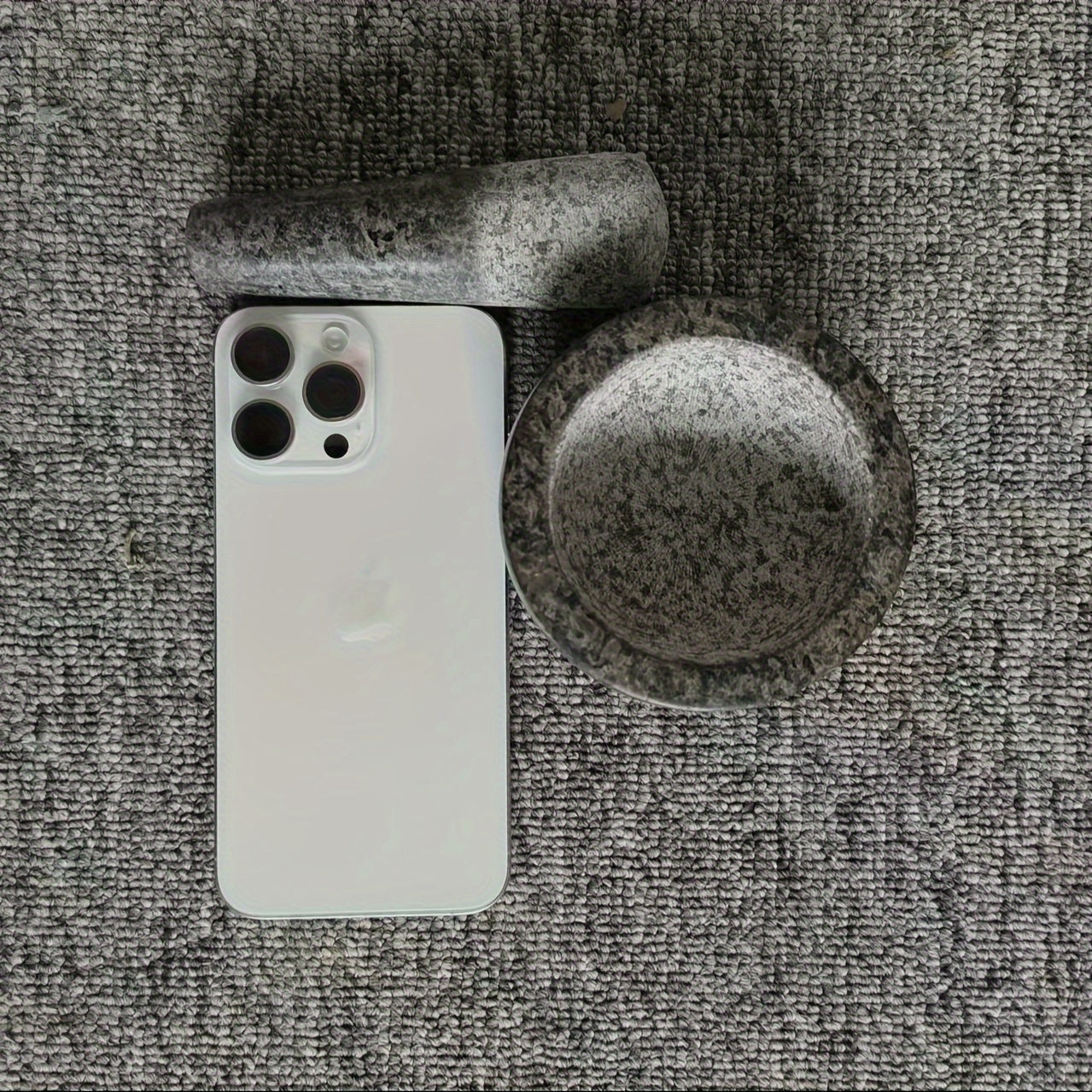 Vue de haut d'un mortier en granit avec le pilon à côté d'un iPhone, montrant la taille du mortier par rapport au téléphone, accessoire de cuisine durable.
