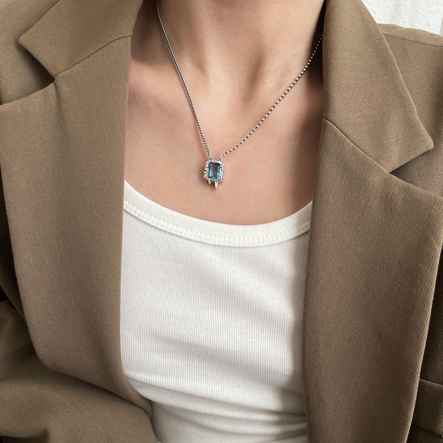 Collier en argent S925 avec zircon bleu sous veste marron.