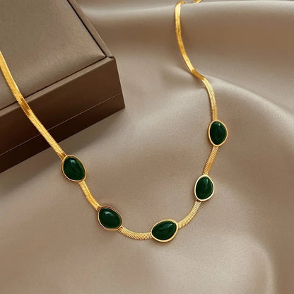 Collier doré en pierre verte déposé à côté de sa boite